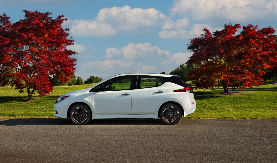A white Nissan Leaf is shown parked by two trees.