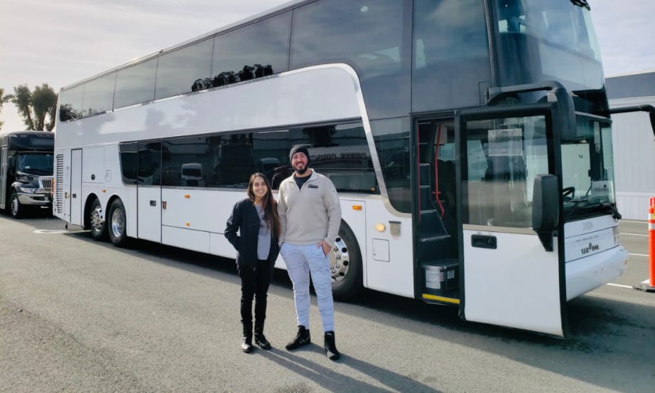 Two people standing in front of a white charter bus parked at a transportation facility.