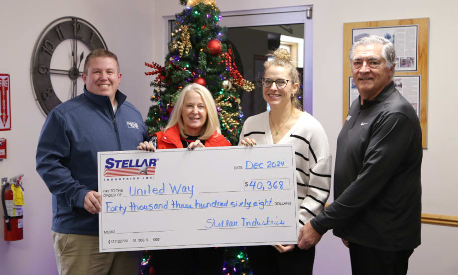 Four business people hold a large symbolic check as part of a charitable donation.