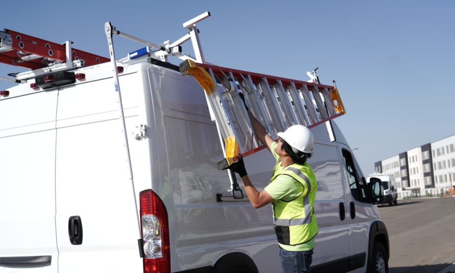 Man unloads ladder of the rack of a work van.