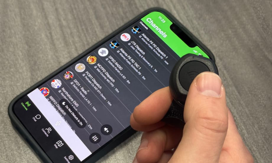 Closeup photo of man's hand using a thumg to push a push to talk button with phone on table.
