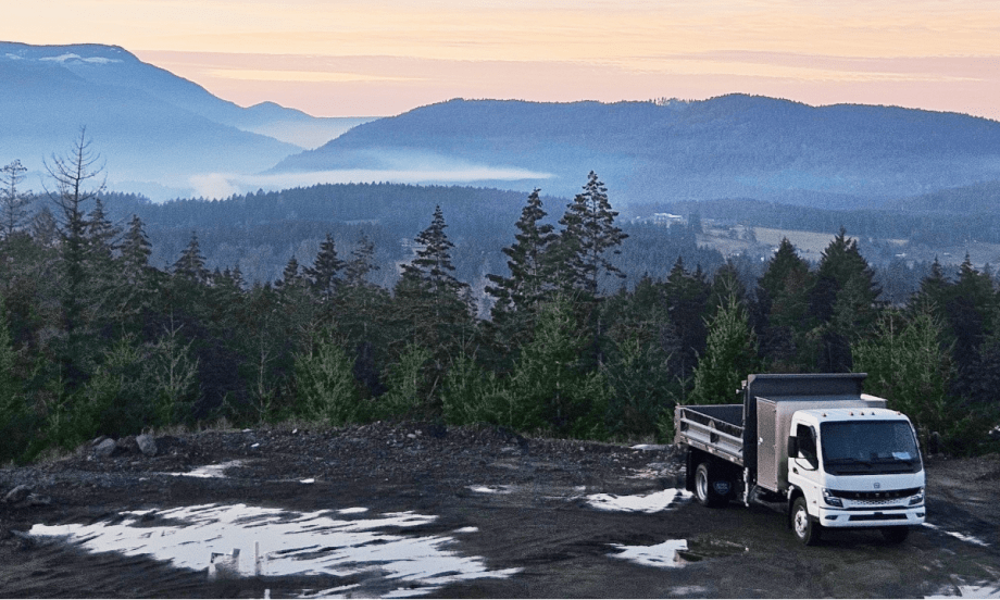 Electric truck parked in front of a scenic mountain background.