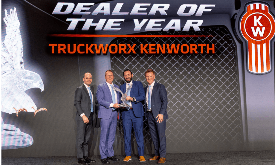 Men in business attire on a stage presenting and receiving an award.