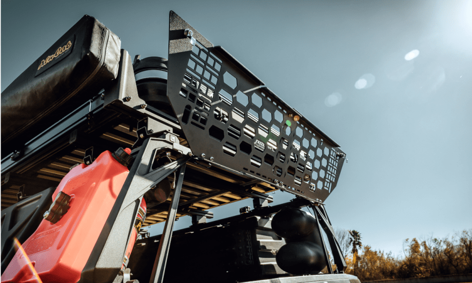 metal gate locks the area above the tailgate of a pickup truck. Photo shows it open against a blue sky.