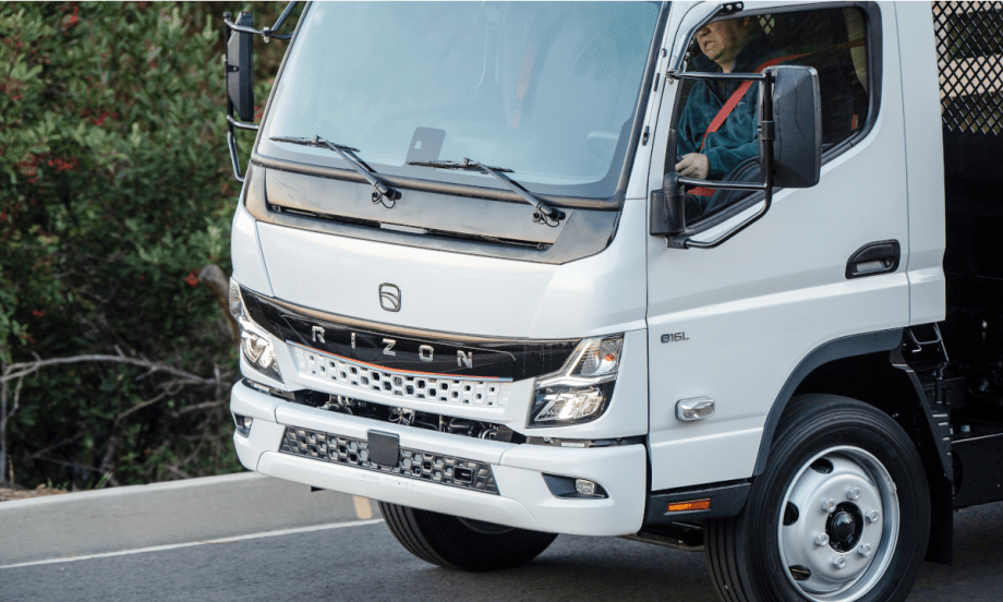 close-up photo of a man driving a white battery electric truck.