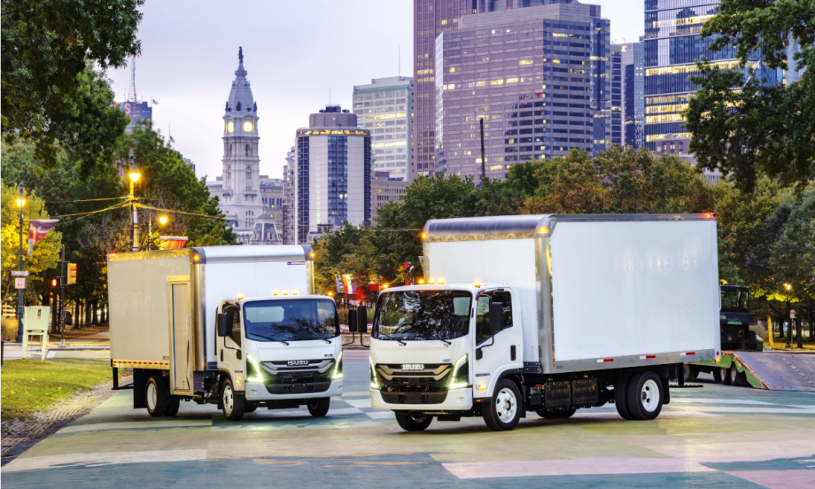 Two white Isuzu box trucks parked with a downtown skyline in the background.