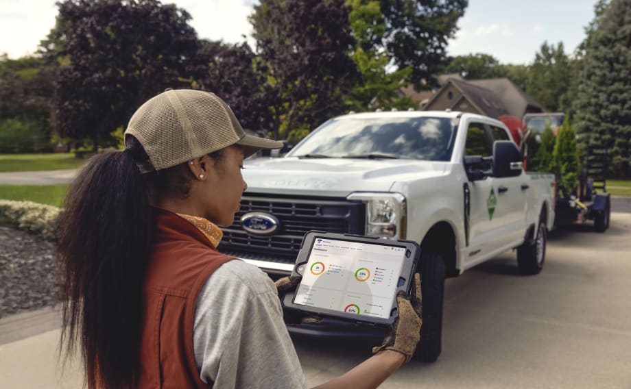 Woman worker looking at telematics on a tablet with a Ford work truck in the background.