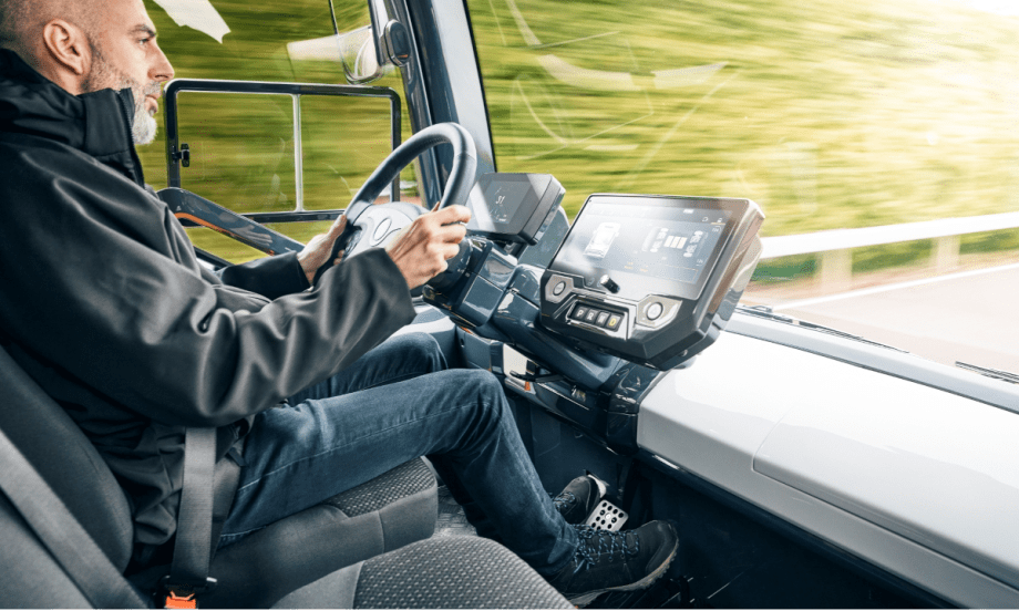Man inside the cab of a futuristic looking truck driving.