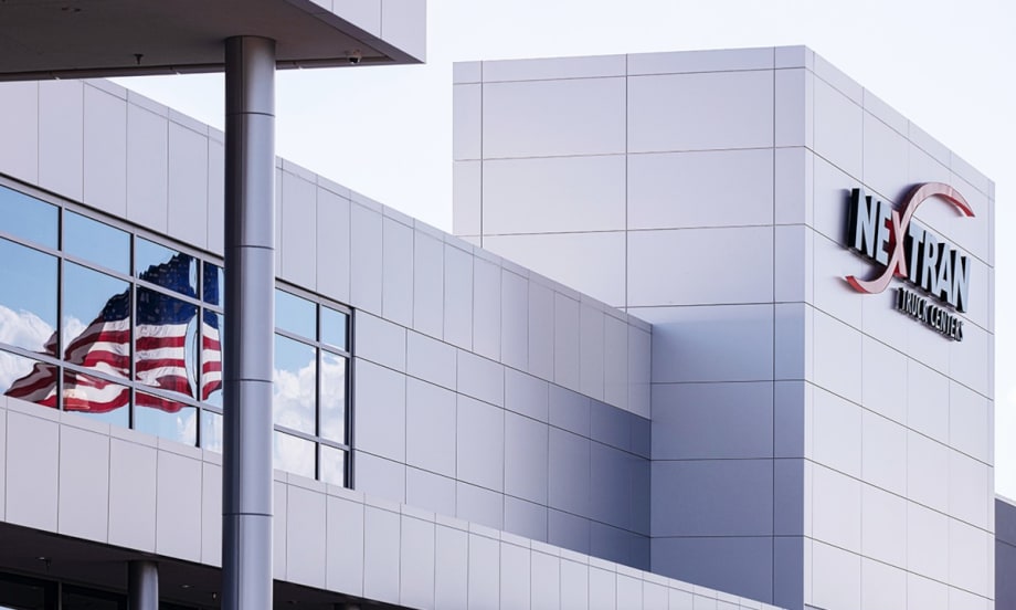 Office building marked by a sign that says Nextran, American flag reflected in a window.
