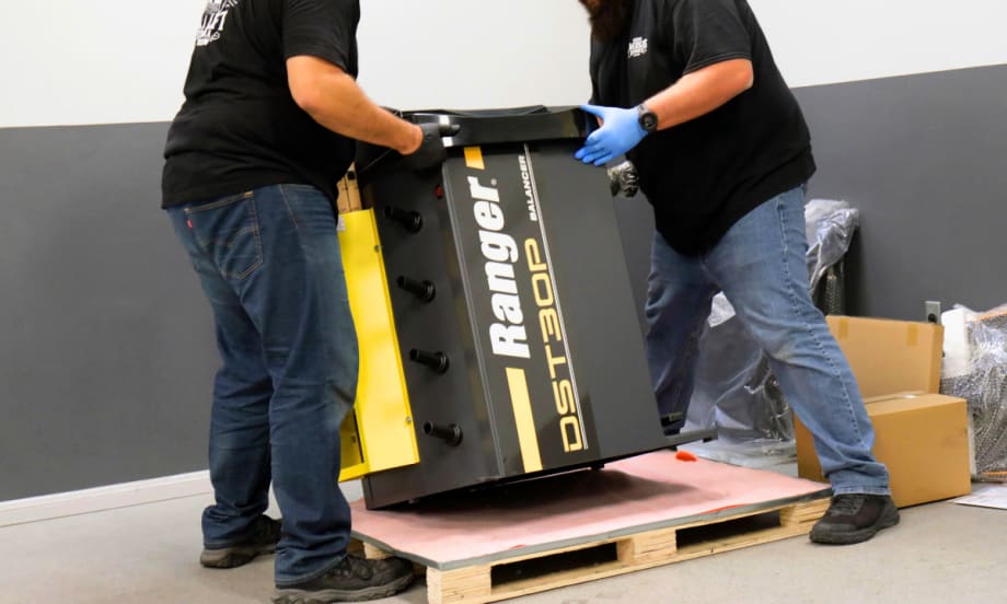 Men lifting a piece of industrial equipment off a wooden pallet.