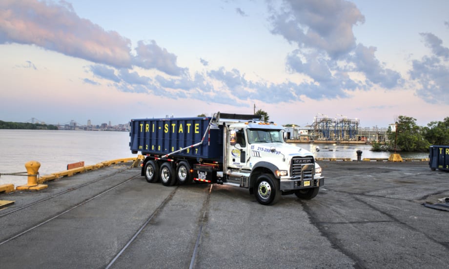 Mack Granite with roll-off container parked in a port area.