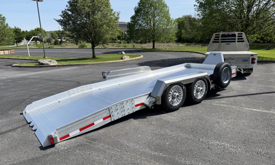 Rear quarter view of an aluminum kneeling trailer hitched to a truck.