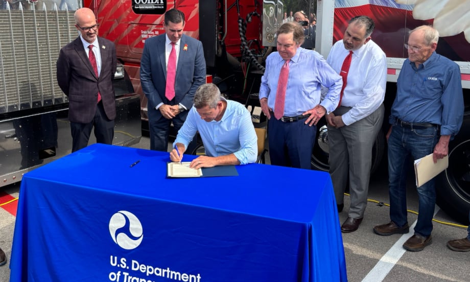 Man seated at a table signing a document sounded by small group of other men.