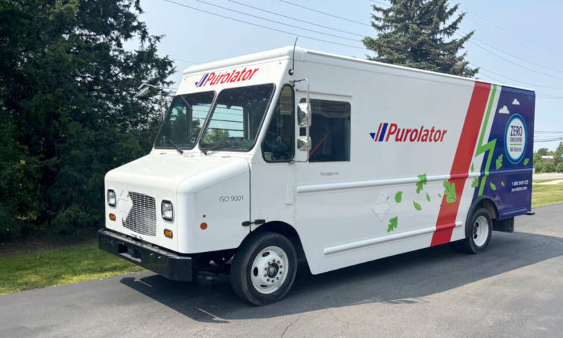 White electric step van with Purolator logo parked in a parking lot.