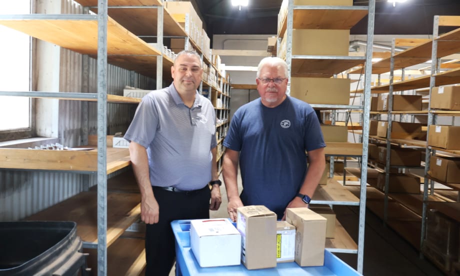 Two men standing in a parts warehouse with shelving and boxes.