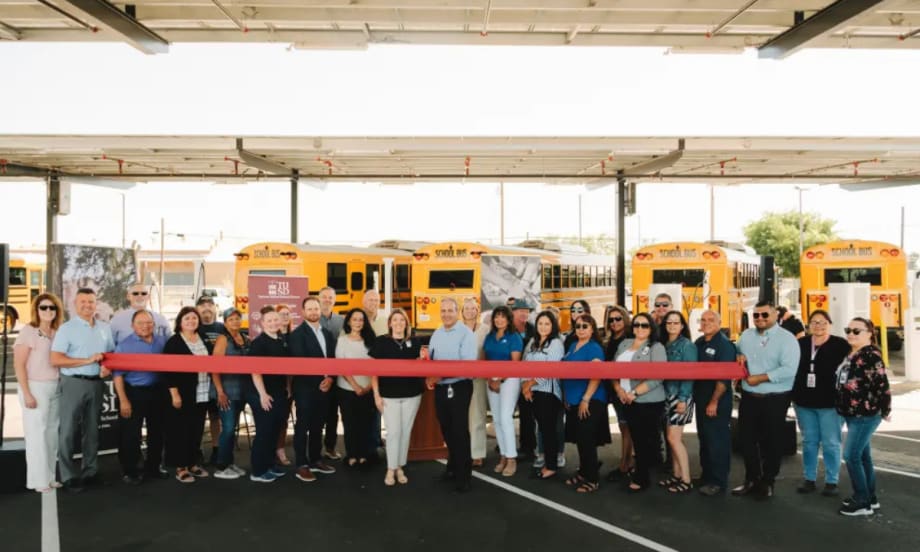 Turlock Unified staff and partners hold a ribbon-cutting in front of new electric school buses under solar canopies at the district transportation center.