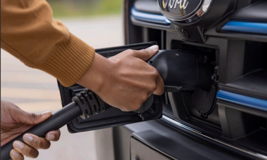 A person plugs a charging cable into the front port of a Ford electric vehicle, highlighting EV charging infrastructure for fleet operations.
