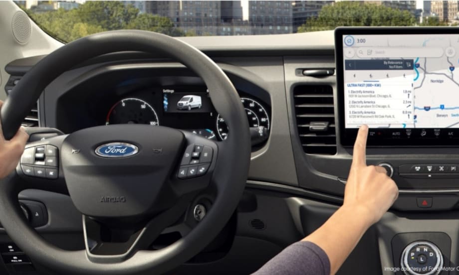 Driver inside a Ford electric vehicle uses the touchscreen navigation system to locate nearby ultra-fast charging stations, illustrating EV operational tools for fleet drivers.