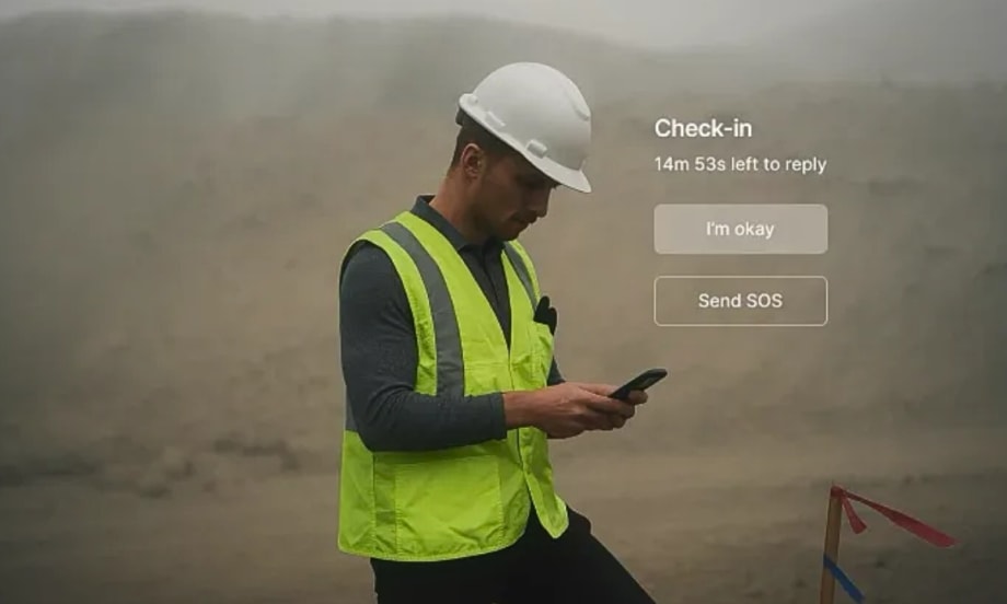 Worker in hard hat and safety vest checks phone with “I’m okay” and “Send SOS” safety check-in options on screen.