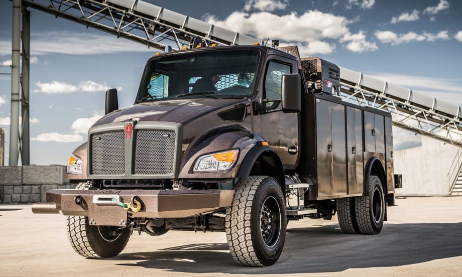 A Kenworth T480 vocational truck with off-road tires and utility service body parked outdoors under a blue sky, showcasing its rugged design for demanding worksite applications.