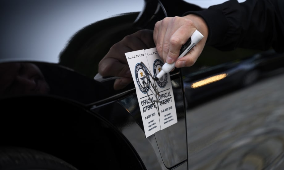 A close-up of a person sealing two Guinness World Records “Official Attempt” stickers on the side of a Lucid vehicle with a marker, reflecting the vehicle's record-setting range attempt.