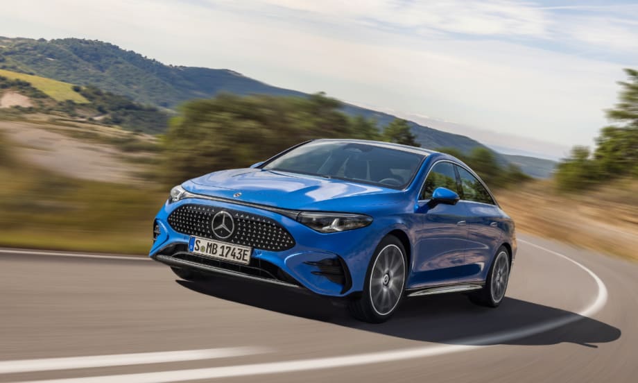 A blue Mercedes-Benz CLA drives on a curving rural road with hills and trees in the background, showcasing its aerodynamic exterior and daytime running lights.