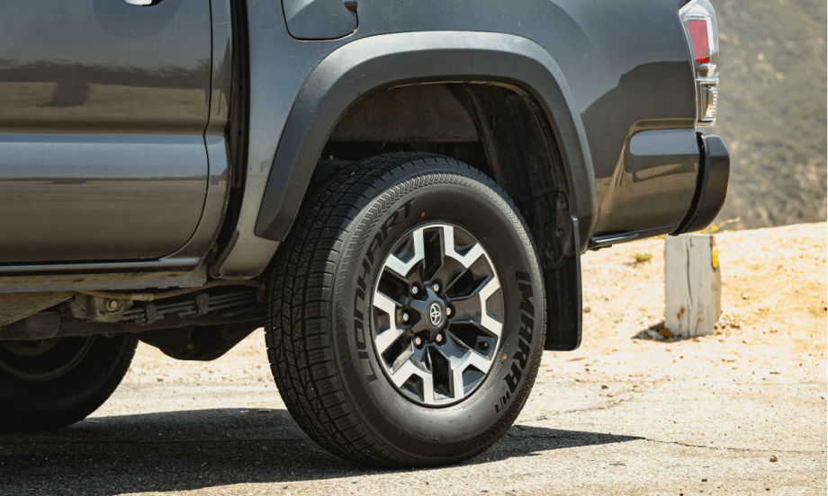 Closeup photo of the rear left tire of a pickup truck parked in a dirt area.