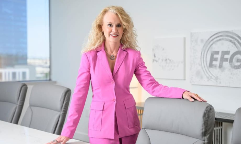 Jennifer Rappaport, CEO of EFG Companies, stands in a conference room wearing a bright pink suit, with the EFG logo visible on the wall behind her.