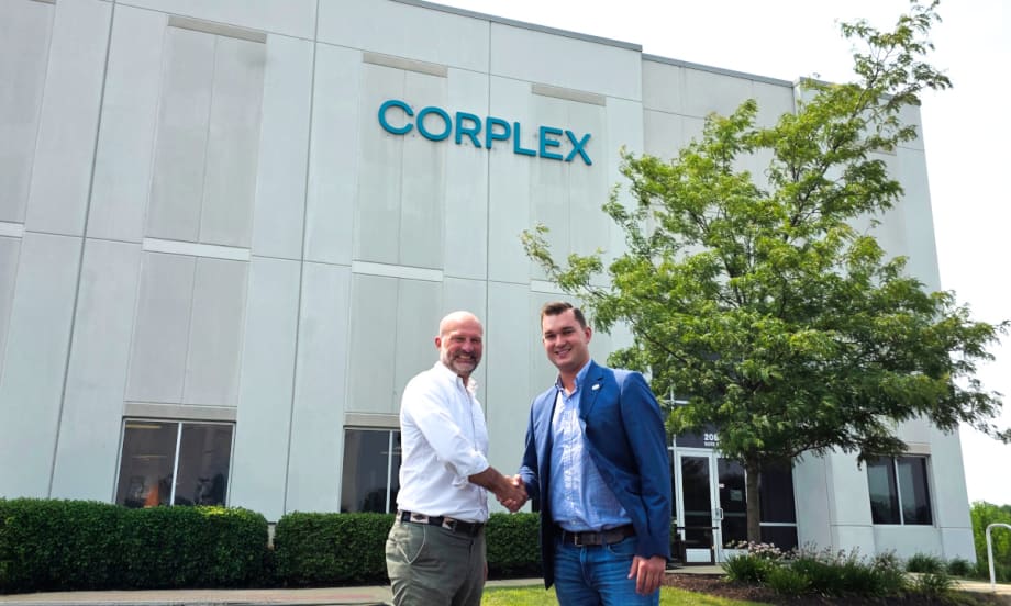 Two businessmen shake hands outside an industrial building with a Corplex name on the upper part of the building.