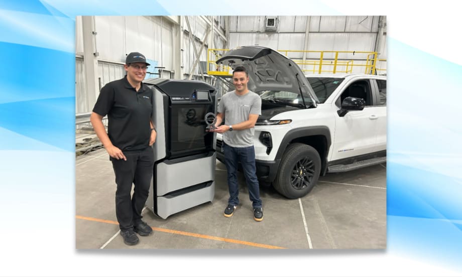 Two GM engineers stand beside a 3D printer holding a trophy, with a white Chevrolet Silverado EV Max Range Work Truck in the background and hood open after a record-setting range test.