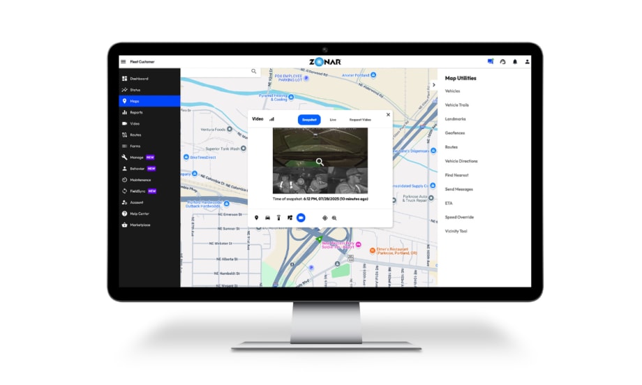 Computer monitor displaying Zonar Ignition’s fleet management interface, showing a city map with vehicle locations and an inset video snapshot from inside a vehicle’s cabin.