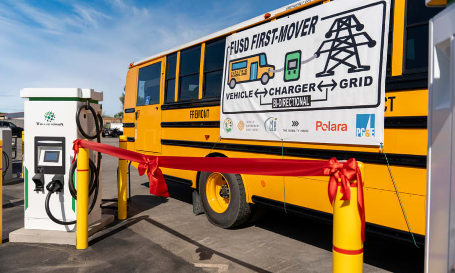 Fremont USD electric school bus next to a Tellus Power bidirectional charger with ribbon, marking launch of V2G system to support grid resilience and clean energy initiatives.
