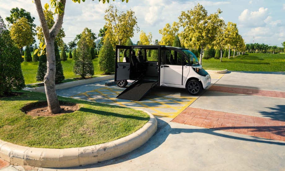 White GEM Wheelchair Accessible Vehicle parked in a handicap space with ramp extended for wheelchair access.
