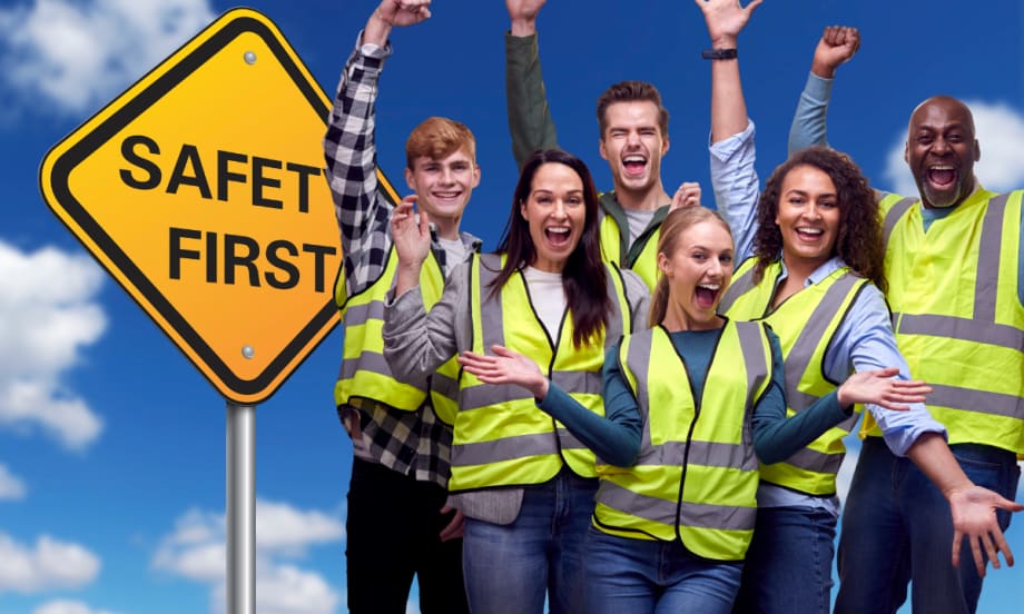 Group of smiling workers in safety vests standing by a Safety First sign, celebrating a strong workplace safety culture.