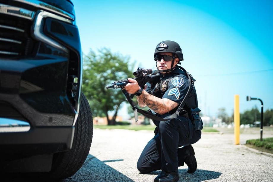 Police officer crouching behind vehicle, holding rifle in tactical stance