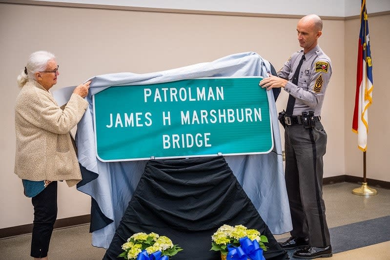 Police officer and elderly woman unveiling Patrolman James H Marshburn Bridge sign