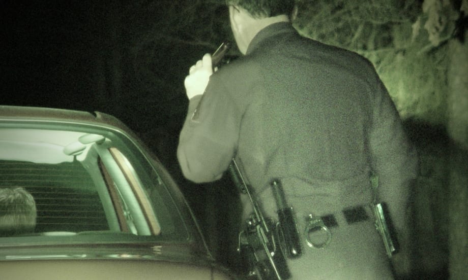Police officer at night standing beside patrol car, viewed from behind