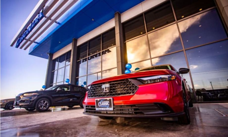 Exterior of the new Classic Honda of Midland dealership with floor-to-ceiling glass, blue Honda entry frame, and vehicles on display, including a red Honda sedan in the foreground.