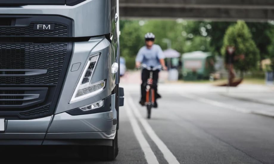 Close-up of a Volvo FM truck front with a cyclist approaching on the road, illustrating Euro NCAP’s focus on truck safety and protection for vulnerable road users.