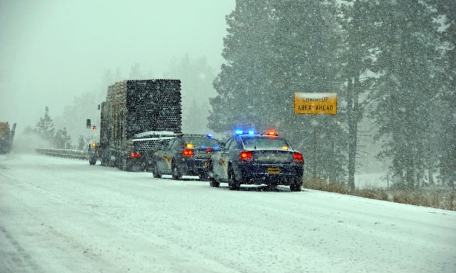 Police vehicles escorting truck on snowy highway during winter storm