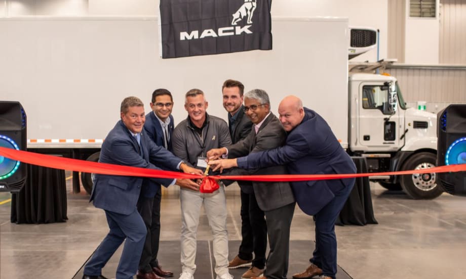 Mack Trucks and TransWestern Truck Centres representatives cut a red ribbon at the opening of the new Calgary dealership with a Mack truck in the background.