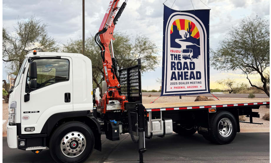 Flatbed Isuzu truck with a sign on back promoting The Road Ahead, the company's annual dealer meeting.