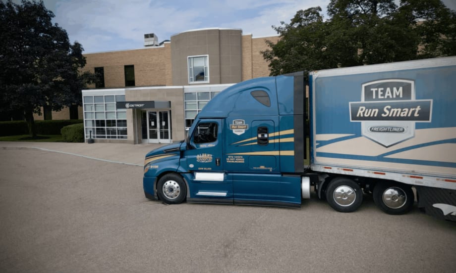 A blue Freightliner Cascadia truck operated by Albert Transport and branded with the Team Run Smart logo parked outside a Detroit Diesel facility.