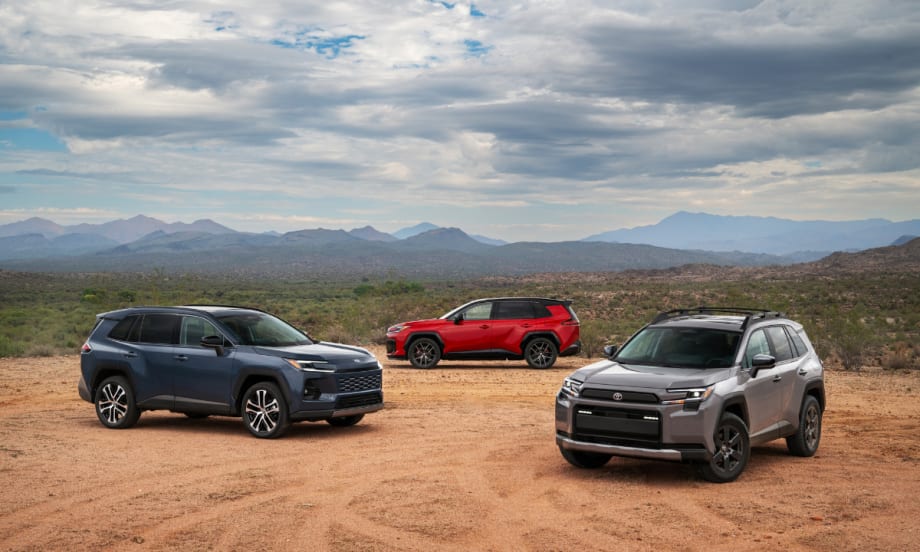 Three 2026 Toyota RAV4 SUVs—gray, red, and blue—parked in a desert landscape with mountains in the distance.