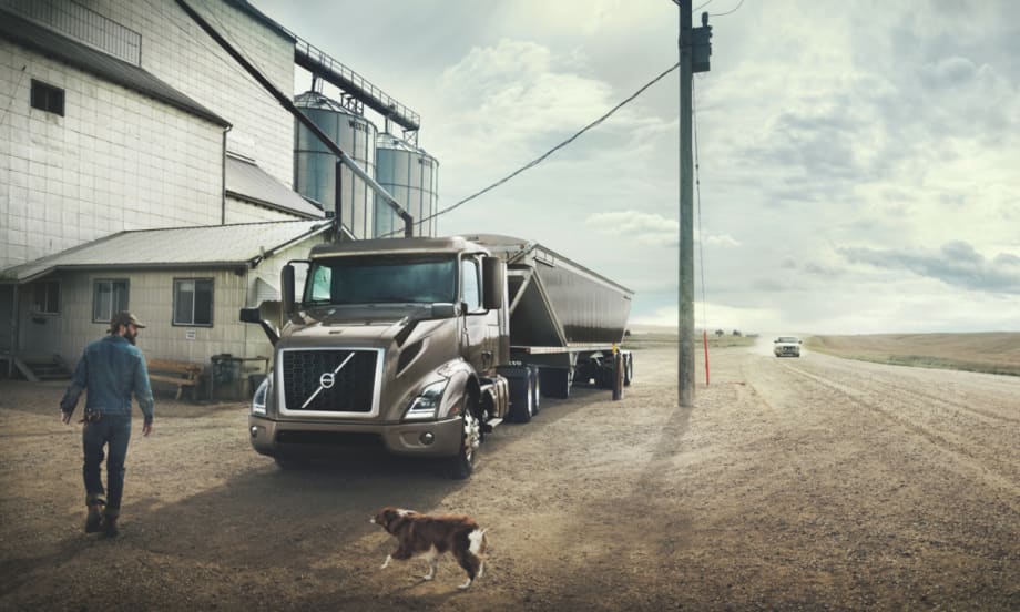 Volvo truck parked at a rural location with a driver and dog nearby.