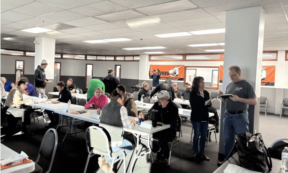Group[ of people working and talking in a classroom setting.