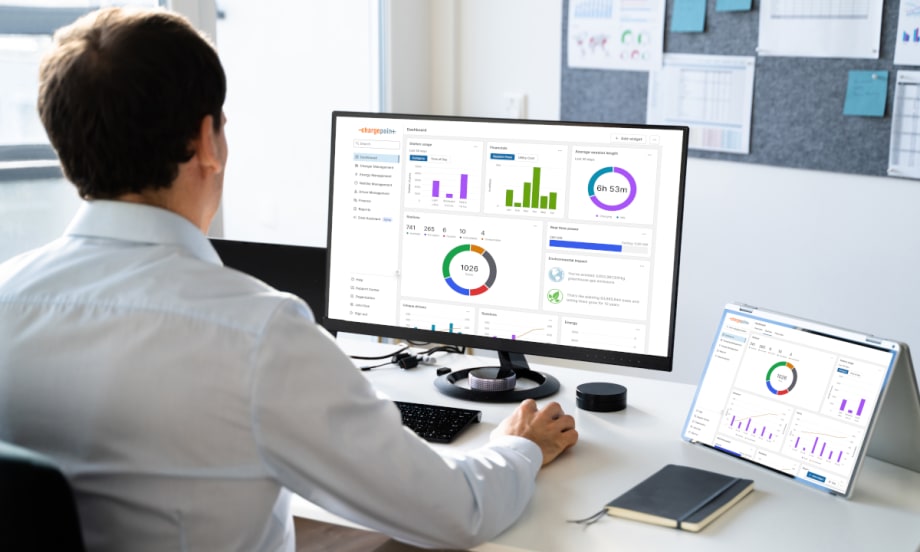 Man seated at desk and looking at charts and graphics on a computer and a tablet.