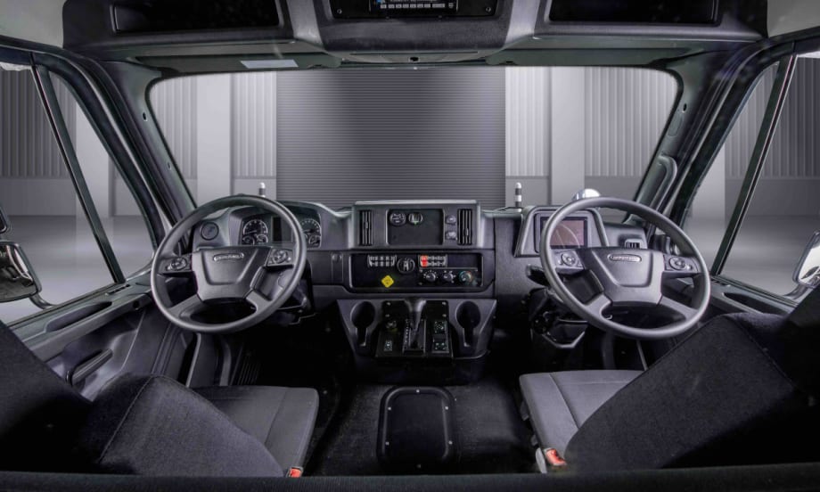 Interior view of a truck cab looking forward toward two steering wheels, one left and one right.