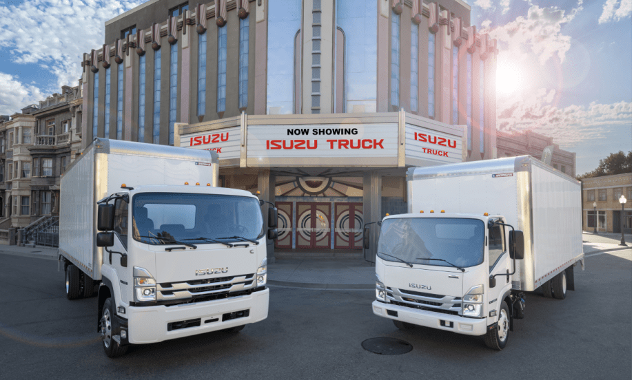Two Isuzu box trucks parked in front of a movie theater with sign that says Now Showing, Isuzu Truck.