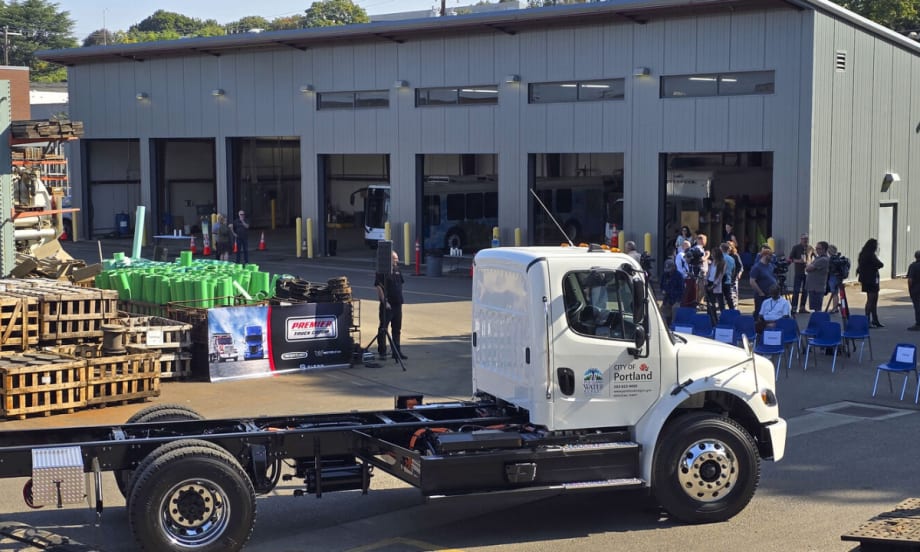 White City of Portland Freightliner eM2 electric truck parked in front of a maintenance building with event seating and attendees in the background.